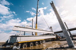 Sundance Equipment Sales. SES wide angle view of industrial heavy duty crane installing precast cement pillars and cement or concrete beams